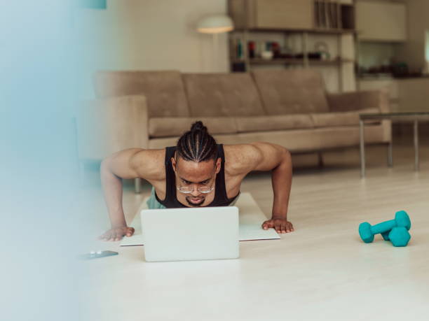 istock Young African American man working push-ups in the living room while watching online training on laptop 1448778645