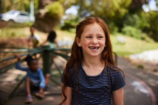 Young girl with no front teeth laughing while playing with friends outside in a park in the summertime
