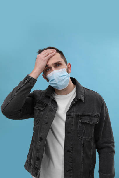 istock Man in mask suffering from headache on light blue background. Cold symptoms 1448779357