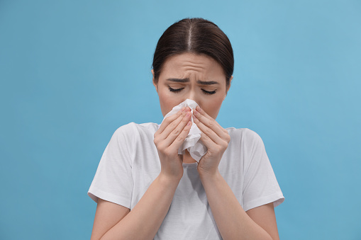 Woman blowing nose on light blue background. Cold symptoms
