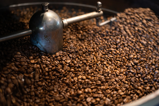 Pile of arabica coffee beans which are roasting and blending in the automatic machine. Food ingredient object background photo. Close-up and selective focus.