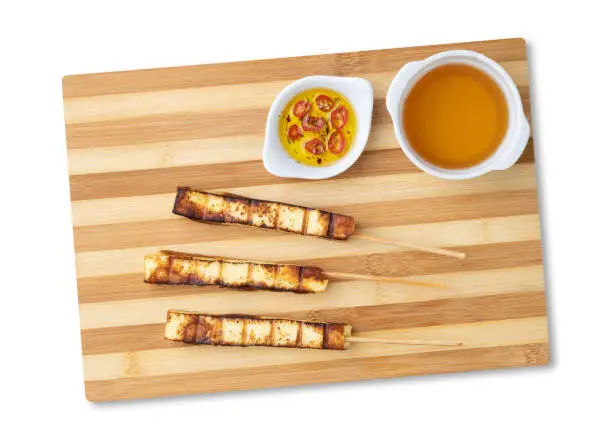 Grilled Rennet or Coalho cheese on a wooden board with sugar syrup and pepper isolated over white background.