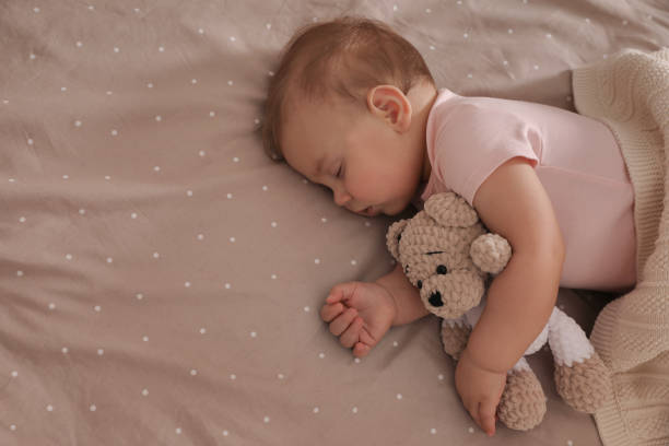 istock Adorable little baby with toy bear sleeping on bed, above view. Space for text 1448781226