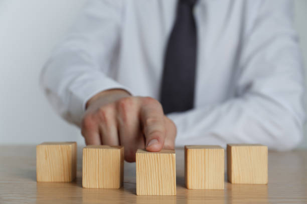 istock Businessman arranging blank cubes on wooden table, closeup. Space for text 1448783632