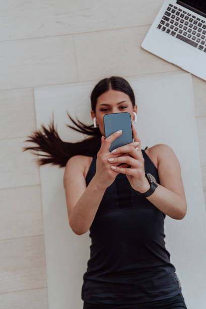 istock Sportswoman using a smartphone while resting and lying on floor of modern house 1448786507