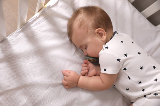 istock Adorable little baby with pacifier sleeping in crib, above view 1448786556