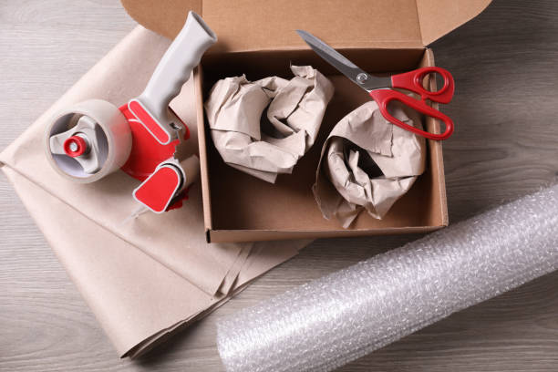 open box with wrapped items, adhesive tape, scissors, paper and bubble wrap on wooden table, flat lay - packaging packing adhesive tape box imagens e fotografias de stock