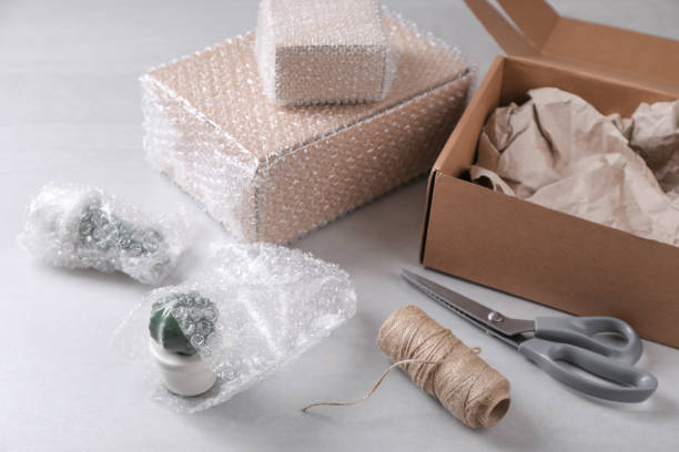 istock Fragile ceramic decor elements in bubble pack near cardboard boxes, scissors and twine roll on light grey table 1448788955