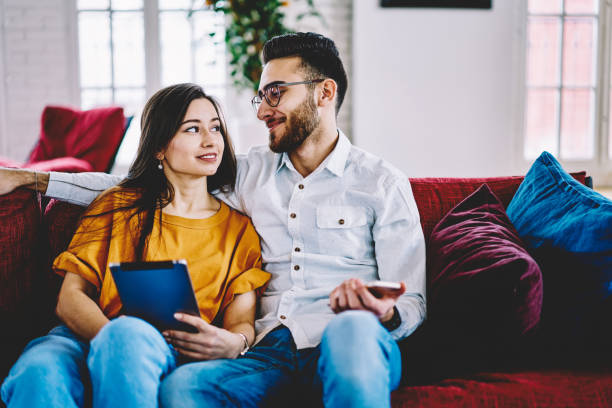 carefree girlfriend and boyfriend discussing content plan during online blogging via smartphone and touch pad, millennial couple in love communicate about social networking while resting in home - armenian ethnicity imagens e fotografias de stock