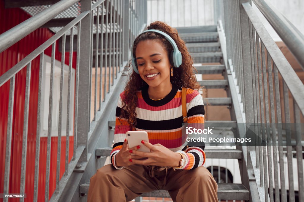Phone, headphones and black woman on stairs in city streaming music, audio or radio. Gen z, earphones and Brazilian student on 5g mobile, texting or internet surfing, social media or web browsing. Generation Z Stock Photo