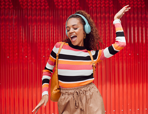Dance, music and freedom with a black woman on a red background outdoor for fun or movement. Radio, streaming and audio with a young female dancing while listening to a playlist on headphones