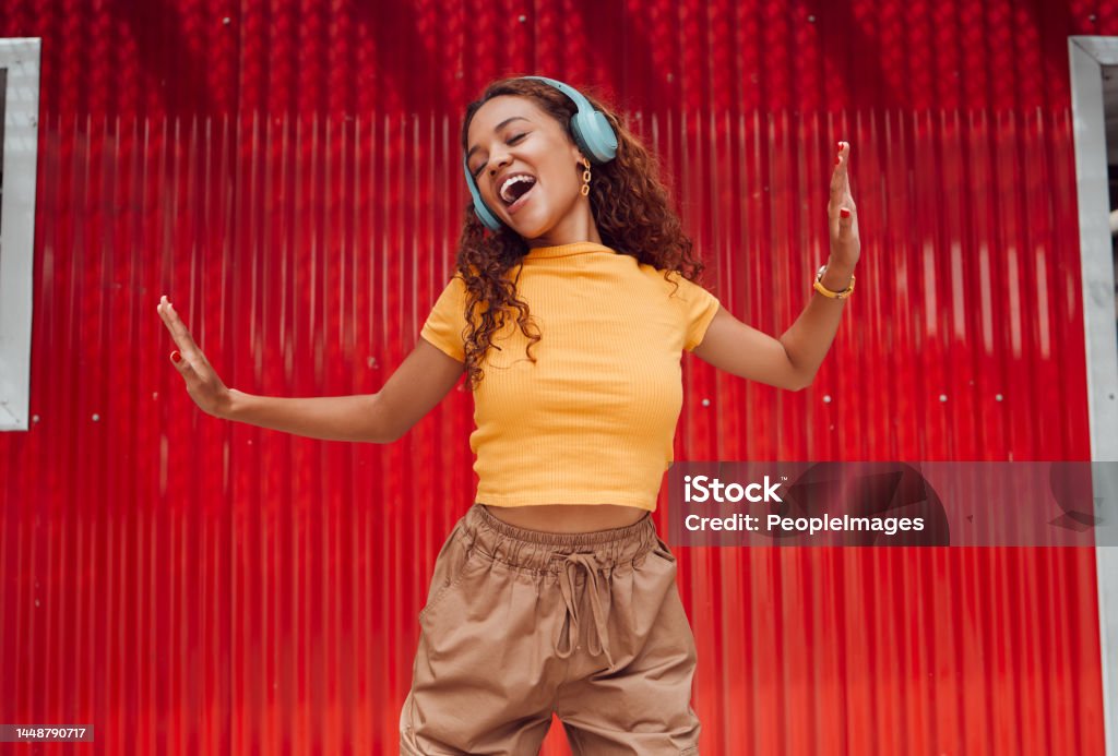 Headphones, black woman and happy dance in city against red building background. Music, dancing and carefree female dancer in Brazil laughing, singing and streaming audio or radio on wireless headset Music Stock Photo