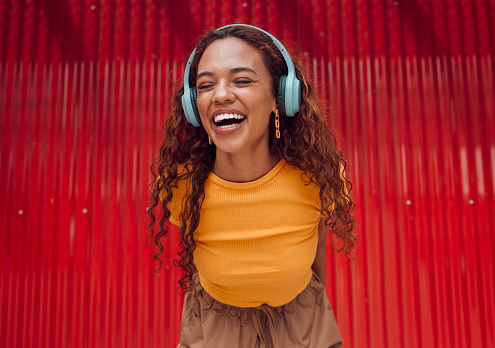 Relax, urban and woman with headphone music enjoying happy rhythm with bluetooth connection. Smile of latino girl listening to feel good streaming while resting at wall for leisure break.