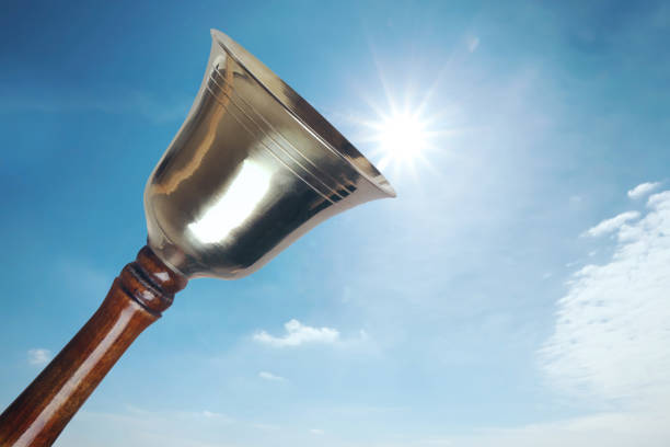 Shiny school bell with wooden handle against blue sky