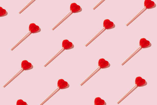 パステル背景に赤いハート型のロリポップパターン。最小限のバレンタインまたは愛のコンセプト。
