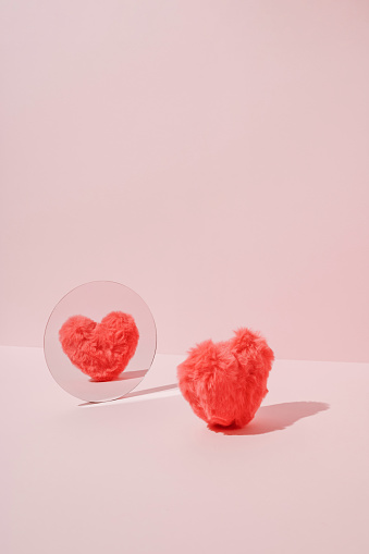 Pink fluffy plush heart reflecting in mirror.  Minimal love or Valentine's concept.