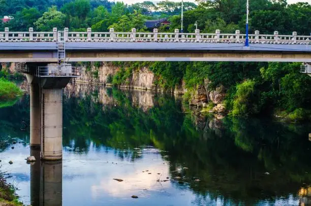 A beautiful bridge over the river Samcheol in South Korea with a reflection of green nature on the surface