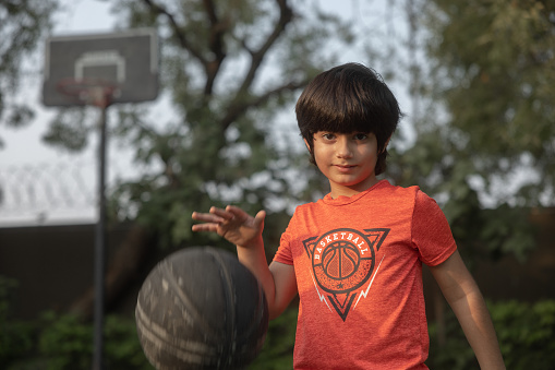 Mixed race (Indian-Iranian) 8 year old playing with his basketball, active lifestyle. Looking at camera smiling