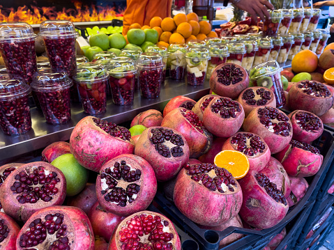 Pomegranate and oranges cut in half on fruit market stall ready to make juice on plastic glasses in Istanbul city. Popular fresh drink in Turkey