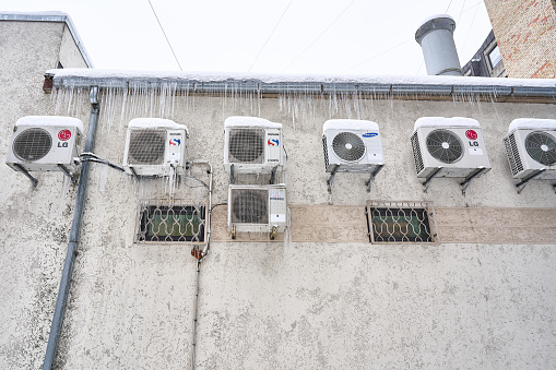 Riga, Latvia - 12 December, 2022: Various brands air conditioners mounted on the wall are frozen and covered in icicles.