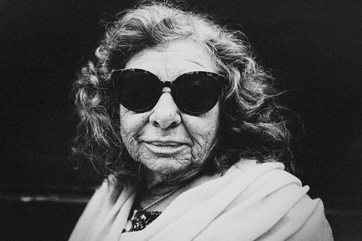 Portrait of an old lady on the street. She wears sunglasses in the style of the 60s.