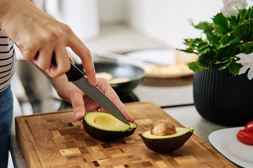 Process of woman cutting avocado for toasts in kitchen interior. Woman preparing healthy breakfast at morning. Vegan food