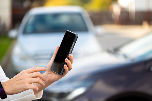 woman with smartphone standing next to the car, using mobile app for online communication, shpping