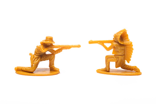 Wild West. Plastic figurines of a cowboy and a native american with guns exchange fire on white background
