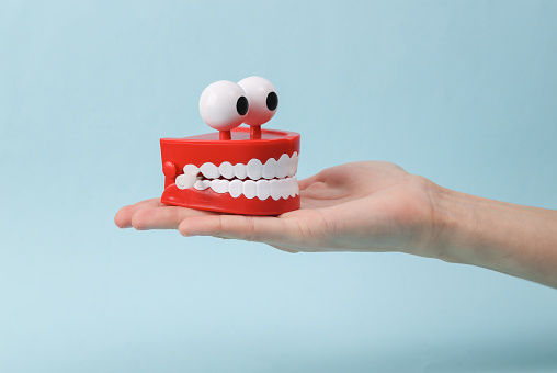 Funny toy clockwork jumping teeth with eyes on palm hand, blue background.