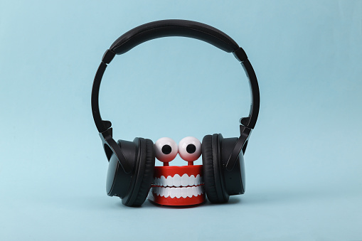 Funny toy clockwork jumping teeth with eyes listen music in stereo headphones on blue background.