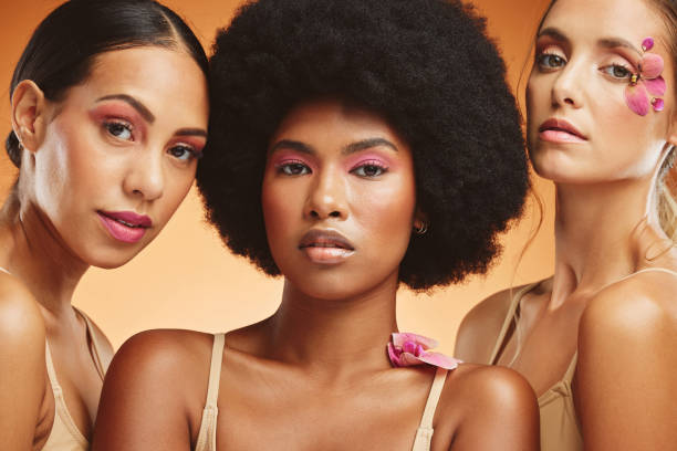 Diversity, beauty and women with flowers for makeup, skincare and cosmetics. Skincare products, spa wellness and group of girls portrait in orange studio with pink orchids for natural beauty products diversidad, belleza y mujeres con flores para maquillaje, cuidado de la piel y cosmética. productos para el cuidado de la piel, bienestar de spa y retrato de grupo de chicas en estudio naranja con orquídeas rosadas para productos de belleza naturales