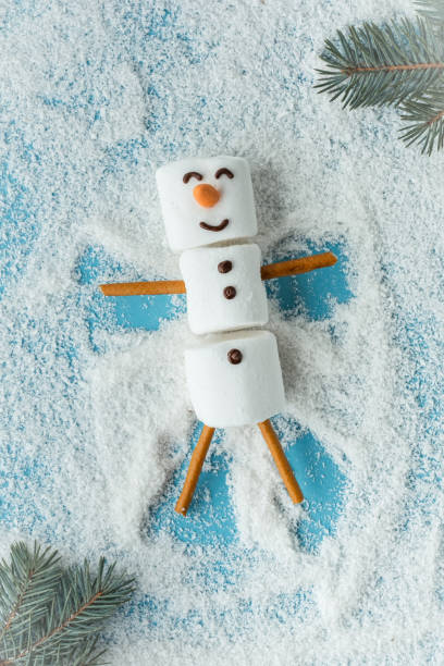 istock Marshmallow snowman on the blue background covered with snow. Flat lay. Copy space. Anticipation of Christmas. Winter concept background 1448821685