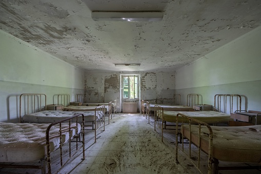 An old abandoned and dilapidated hospital with many beds with windows in the background