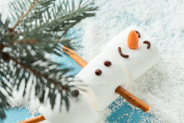 istock Marshmallow snowman on the blue background covered with snow. Flat lay. Copy space. Anticipation of Christmas. Winter concept background 1448823912