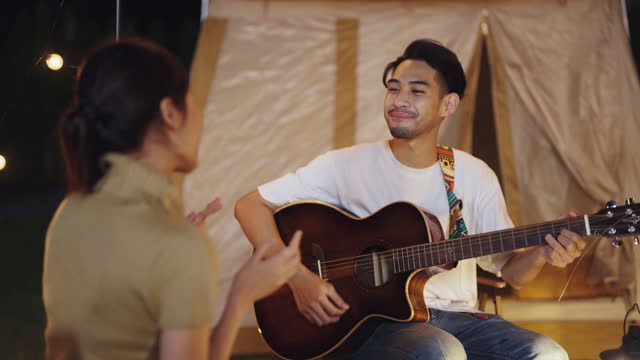 Asian young couple playing guitar during camping on holiday