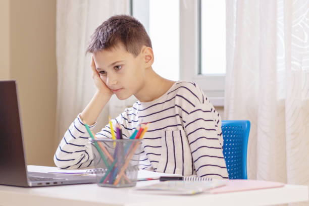 istock Sad tired boy sitting at table with books and laptop computer at home. Learning difficulties, online education concept 1448833438