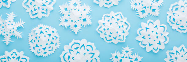 istock Different white snowflake shapes created from paper on light blue table background. Pastel color. Closeup. Top down view. Handmade decoration elements for winter festive. Wide banner. 1448833676