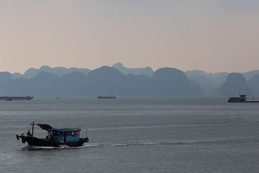 Small boats ply their way through the impressive karst landscape that makes up the famous Ha Long bay, Vietnam