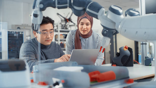 istock In Technology Research Facility: Young Female Specialist Talks With Asian Engineer. They Have A Discussion and Point at Laptop Screen. Professionals Work on Modern Autonomous Factory Optimisation. 1448837344