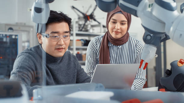istock In Technology Research Facility: Young Female Specialist Talks With Asian Engineer. They Have A Discussion and Point at Laptop Screen. Professionals Work on Autonomous Factory Optimisation. 1448837357