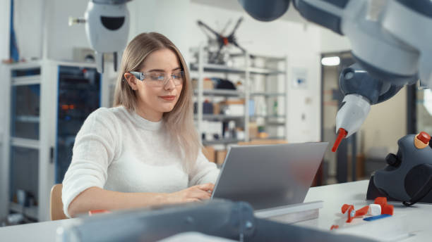 istock Female Automation Engineer Writes Code on Laptop and Moves Bionic Claw At the Factory. Modern and Futuristic Robotic Equipment Starts the New Era in Computer Science Industry Concept. 1448837637