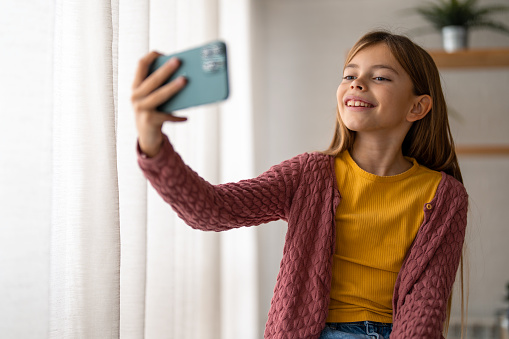 Young little girl having fun at home taking a self portrait on a smartphone.