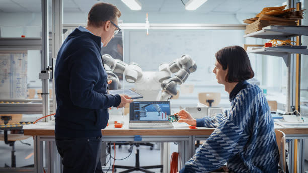 istock Computer Design Student Talk with Teacher in University Of Technology and Hold Microchip while Creating Computer Program For Robotic Arm. Breakthrough in Modern Technology Concept. 1448839821