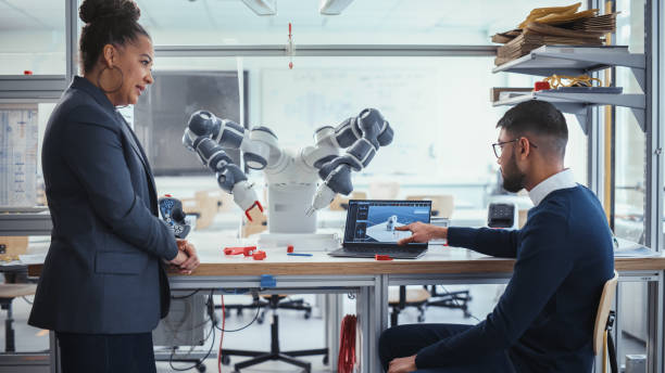 istock Black Chief Engineer Discussing Futuristic Robotic Arm with Young Promising Male Computer Scientist with Laptop in the Research Laboratory. Innovative Startup Company Concept. Medium Shot. 1448840093