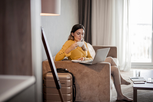 Businesswoman in the hotel room holding cup of tea while working