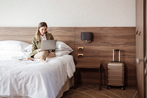 Businesswoman sitting on hotel room bed and using laptop during business trip