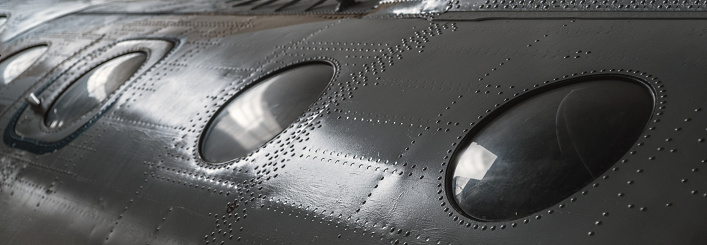 A number of portholes in the body of the vehicle. Metal texture with rows of rivets. Selective focus.