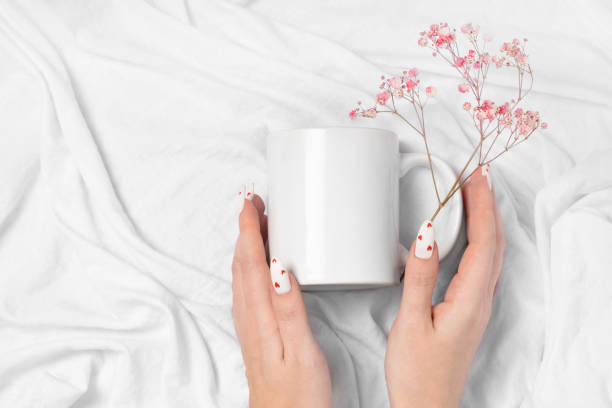 Female hands hold mock up white empty mug on a textile background, cup for Valentine's Day manicure