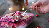 Homemade New Year is a herring salad under a fur coat on a wooden background. A man's hand lays a Russian traditional Christmas salad with a spoon.