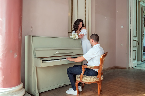 The groom sits at the piano and plays the bride a cheerful melody